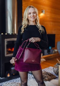 Burgundská kožená kabelka se strukturovaným designem, odnímatelným popruhem a stříbrnými kovovými detaily. Hladká textura s logem na přední straně.