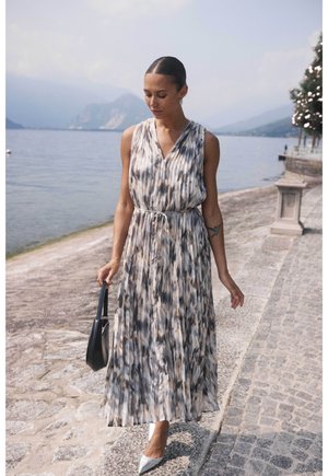 Robe plissée sans manches dans des tons doux de bleu et beige, avec un décolleté en V et une taille cintrée. Associée à des escarpins argentés pointus et à un sac noir.