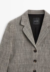 Grå mønstret blazer med en hakket revers, to sorte knapper og en glat inderforing. Mærkat synlig med "Massimo Dutti" branding.