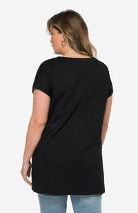Camiseta negra de manga corta con un corte relajado, que presenta un escote redondo y una textura suave. Combinada con jeans de color azul claro.