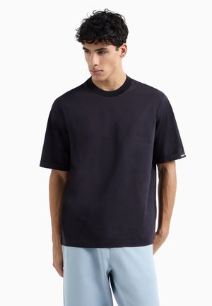 T-shirt navy a maniche corte in un morbido misto cotone, con collo a costine e un sottile dettaglio di branding sulla manica. Tessuto morbido.