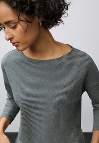Ränder långärmad topp i grått med båtformad halsringning, strukturerat tyg och figursydd design som framhäver horisontella linjer.