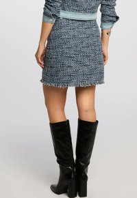 Blauwe tweed mini-jurk met een gefranjeerde zoom, gecombineerd met knielange zwarte leren laarzen. De jurk heeft een textuur van geweven stof.