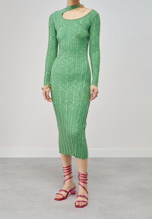 Grünes, geripptes Strickkleid mit langen Ärmeln und einem Schlüsselloch-Ausschnitt. Kombiniert mit pinken Sandalen mit spiralförmigen Riemen und Blockabsätzen.