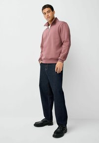Polarowa bluza w odcieniu przybrudzonego różu z połową zamka błyskawicznego, w zestawieniu z ciemnoniebieskimi dżinsami i czarnymi sznurowanymi butami.