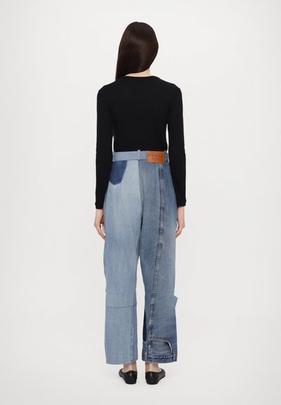 Denim-housut, joissa on ainutlaatuinen suunnittelu, jossa on kontrastisia vaalean- ja tummansinisiä osia, leveä vyötärönauha ja nahkätagi, jossa lukee "AWAKE MODE."