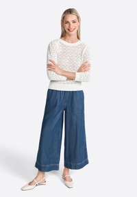 Maglione bianco lavorato a maglia con scollo rotondo e maniche lunghe, abbinato a pantaloni in denim scuri a gamba larga e ballerine beige.