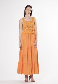 Maxi kjole i lys orange bomuld med hæklede detaljer, firkantet halsudskæring og lagdelt skørt. Glat tekstur og luftig design.