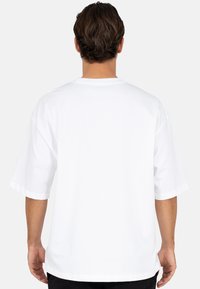 Witte oversized T-shirt met korte mouwen, ronde hals en een gladde textuur. De achterkant is effen zonder zichtbare afbeeldingen of versieringen.