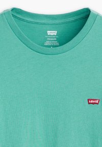 Turkizna bombažna majica s ribanim ovratnikom in malim rdečim logotipom Levi's na levem prsnem delu. Standardni kroj, mehak na otip.