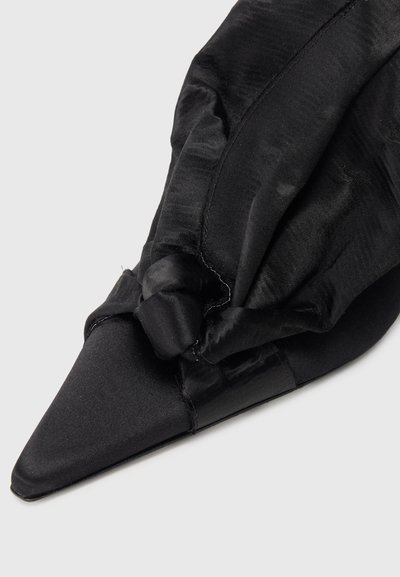 Sapato de salto em cetim preto, com um detalhe de tecido em nó na parte superior. Apresenta um design elegante e uma textura suave.