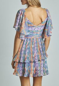 Kurzärmliges, lila gemustertes Kleid mit Rüschensaum, das geometrische Designs in Pastellfarben zeigt; der Stoff wirkt leicht und luftig.