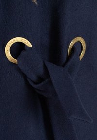 Marine wol stof met een grote gouden accentgrommet en een gestrikt stofdetail, met een zachte textuur en schone randen.