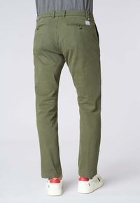 Chino verde oliva con una vestibilità slim, caratterizzati da un tessuto testurizzato, passanti per la cintura, due tasche posteriori, abbinati a sneakers bianche.