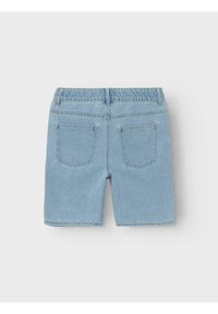 Shorts de mezclilla de color azul claro con cintura de altura media, banda elástica en la cintura y dos bolsillos traseros. Las piernas terminan justo por encima de las rodillas.