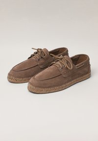Brown suede boat shoes with round laces, metal eyelets, and braided rope soles. The design features a rounded toe and a low profile.