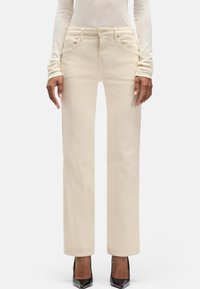 Jasnobeżowe proste dżinsy z miękkiej bawełny z tonującymi szwami, pięcioma kieszeniami i talią średniego wzrostu. Na stopach czarne wysokie obcasy.