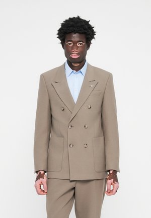 Double-breasted beige suit jacket made of textured fabric, paired with a light blue shirt, featuring two front pockets and button details.