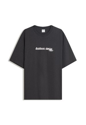 T-shirt nera oversized con testo in corsivo bianco "laidback stories" e una piccola grafica di un globo sul petto.