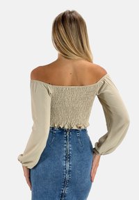 Haut beige à épaules dénudées avec un dos smocké, des manches ballon longues et un ourlet volanté, associé à une jupe en denim taille haute.