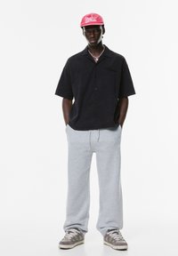 Cămașă neagră cu mâneci scurte, pantaloni de trening gri deschis, adidași gri și o șapcă roz cu logo alb. Design simplu, croială lejeră.