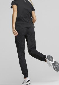 Svart träningsoutfit med en åtsittande kortärmad topp och avsmalnande byxor med en elegant design, kompletterad med texturerade, mönstrade träningsskor.