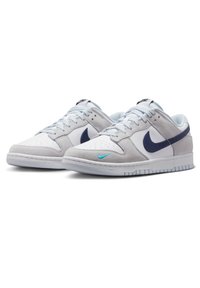 Vita och ljust grå sneakers med marinblå accenter, mocka och texturerade material, perforerat tårum och en turkos Nike-logotyp.