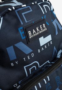 Ruksak s geometrijskim uzorkom u plavoj i bijeloj boji na crnom platnu. Teksturirana površina s crnom etiketom na kojoj piše "BAKER BY TED BAKER."