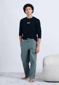 Cămașă neagră cu mâneci lungi, cu textul "BOSS" și pantaloni verzi cu carouri. Material moale, croială lejeră și logo vizibil pe talie.