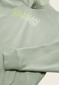 Sudadera verde claro hecha de material suave, con un bolsillo canguro, puños acanalados y texto gráfico en blanco y verde neón en el pecho.