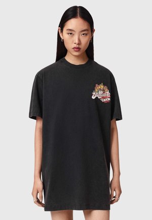 Ung kvinde med langt mørkt hår iført en løs sort T-shirt kjole med blomsterprint og tekst på brystet.