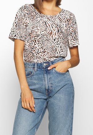 Woman wearing a short-sleeve, animal print top tucked into high-waisted light blue jeans with one hand in pocket.