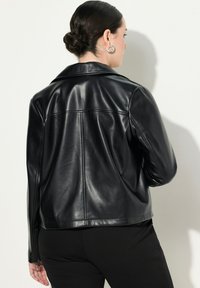 Musta nahkatakki, jossa on muotoiltu kaulus, sileä pinta ja vetoketju takana. Siistit linjat ja istuva malli.