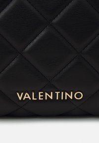 Black quilted leather bag with gold "VALENTINO" logo. Features diamond-shaped stitching and smooth texture.