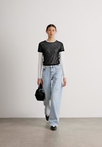 Top de rayas blancas y negras de manga corta sobre una camisa blanca de manga larga, combinado con unos vaqueros anchos de pierna rota en un tono azul claro y un bolso negro.