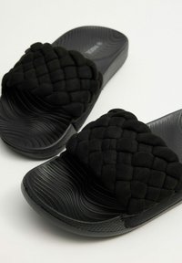 Chanclas negras con una correa de ante trenzada, plantilla texturizada con surcos y una suela de goma lisa.