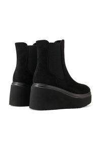 Stivaletti ankle in suede nero con pannelli laterali elasticizzati e suola spessa. Presentano un tacco alto a forma di cuneo e una texture liscia.