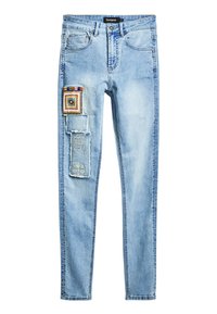 Un jean en denim bleu clair présente un design ajusté avec des patches décoratifs et des broderies sur la cuisse gauche. Il comprend des poches standards.