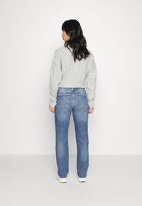 Sweater cinzento cropped, jeans azuis de perna reta com bolsos traseiros e ténis brancos. Textura suave, design casual e denims de lavagem clara.