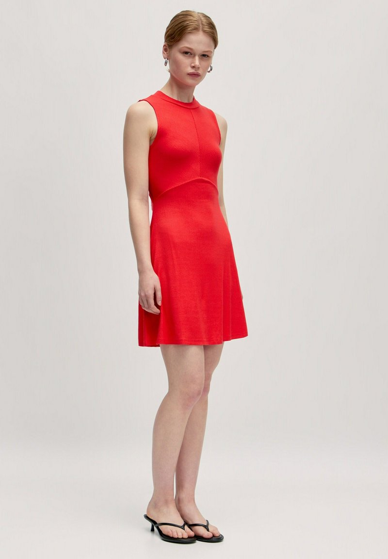 Rotes, geripptes, ärmelloses Kleid mit hohem Kragen, figurbetontem Oberteil und ausgestellt Rock. Es hat eine glatte Textur und ein minimalistisches Design.