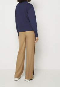 Námořnická mikina s kulatým výstřihem a žebrovaným lemem, spárovaná s béžovými kalhotami s širokými nohavicemi, které mají námořnické boční pruhy a bílé sportovní boty.