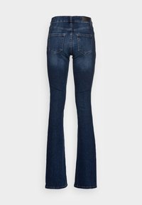 Tmavě modré zvonové džíny s vysokým pasem, které mají dvě zadní kapsy a kontrastní prošívání. Látka má denimo textura.