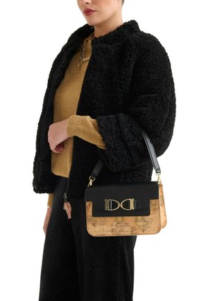 Giacca in pelliccia sintetica nera, maglione dorato, pantaloni neri con brillantini, che tiene una borsa a stampa mappa multicolore con dettagli dorati e accenti neri.