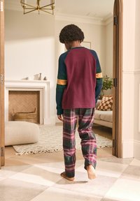Maroon long-sleeve shirt with blue, green, and yellow accents; plaid pants in red, green, and navy. Indoor setting with soft decor.