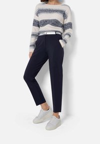 Navybyxor med skräddarsydd design och bältesdetalj, parat med en mönstrad stickad tröja i kräm och marinblått, samt vita sneakers.