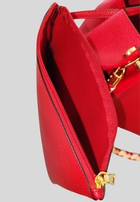 Borsa a mano in pelle rossa con finitura strutturata, caratterizzata da una cerniera in oro e cuciture nere, con una tasca con cerniera aperta.
