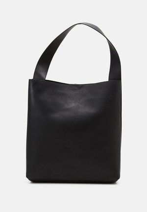 Sac cabas en cuir noir avec une large bandoulière et un design lisse et minimaliste sur un fond uni.
