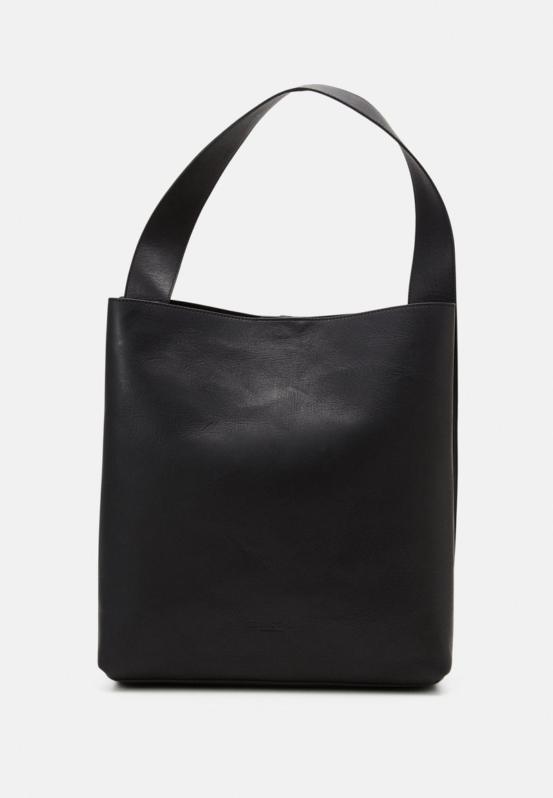 Sac cabas en cuir noir avec une large bandoulière et un design lisse et minimaliste sur un fond uni.