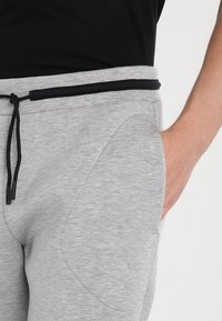 Grå bomullsjoggingbyxor med dragsko i midjan, med sidofickor och en slät, mjuk textur. Det finns svarta detaljer i midjebandet.