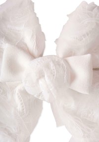 Fiocco di tessuto bianco con trame di tulle e pizzo a strati. Presenta un nodo centrale con ampie code di nastro morbido e bordi delicati e sfilacciati.